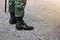 The leg of a soldier wearing black boots stood on an outdoor cement floor.
