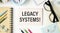 LEGACY SYSTEMS is written in a white notepad