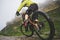 Legs of bicyclist and rear wheel close-up view of back mtb bike in mountains against background of rocks in foggy