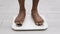 Legs of black girl standing on scale to measure weight. African American Female bare feet with weight scale at home