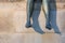 Legs of a bronze sitting statue in front of beige stone background