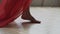Legs of caucasian girl wearing red long dress walking barefoot on floor in the room, . Woman walks pass camera slow