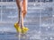 Legs of a child in yellow rubber shoes running through the refreshing splashes of the city fountain on a hot summer day