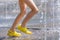 Legs of a child in yellow rubber shoes running through the refreshing splashes of the city fountain on a hot summer day