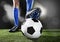 Legs and feet of football player in blue socks and black shoes posing with the ball playing on green grass