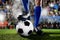 Legs and feet of football player in blue socks and black shoes standing with the ball playing match at soccer stadium