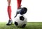 Legs feet of football player in red socks and black shoes posing with the ball playing on green grass pitch