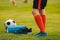 Legs of a football player boy in boots cleats with a ball and foam roller on the green lawn of the stadium