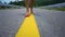 Legs of a girl walking along the roadway along a yellow dividing strip.