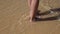 Legs of girl walking barefoot along wet sand beach.