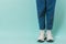 Legs of a girl in white socks, white sneakers and jeans on a blue background. Place for text