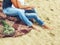 Legs in jeans, men and women sitting on a plaid blanket on the sand on the beach