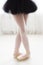 Legs of little balerina wearing pail pink pointe shoes with ribbons