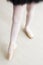 Legs of little balerina wearing pail pink pointe shoes with ribbons