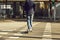 Legs of a man in jeans and sneakers on an electric scooter at a crosswalk on a city street