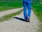 Legs of a man walking country road between vibrant green spring fields. Concepts of freedom, relaxing and active lifestyle