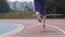 Legs in red snikers of a young woman athlete who starts running at the city athletics track during training in slow