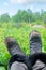 Legs in shabby work boots of man that relax at garden with green forest background