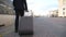 Legs of successful businessman in suit walking along platform and pulling suitcase on wheels. Young confident man with