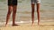 Legs of two young ladies spend summer vacation time strolling on white sandy beach