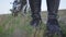 Legs of an unrecognized biker in black leather pants and sneakers standing on the grass in the field. Motorcyclist on