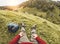 Legs view of man trekker sitting on grass with countryside hills panorama at sunset - Sport, nature and healthy lifestyle concept