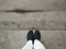 Legs in white trousers, feet in black weave shoes standing on dirty concrete floor