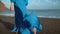 Legs of a woman in beautiful blue dress walking along a black volcanic beach. Slow motion
