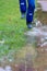 Legs of a young boy in blue waterproof raincoat and rain boots is jumping in deep puddles on a rainy day with happiness in splash