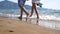 Legs of young couple stepping together along beach at ocean background. Pair walking near sea and splashing water