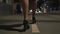 The legs of a young woman walking along the sidewalk of the night city.