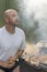 leisure, food, people and holidays concept - happy young man cooking meat on barbecue grill at outdoor summer party. vertical phot