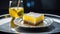 A lemon bar served on a silver platter with a crystal glass filled with sparkling water