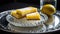 A lemon bar served on a silver platter with a crystal glass filled with sparkling water