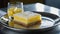 A lemon bar served on a silver platter with a crystal glass filled with sparkling water