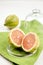 Lemon cut in half with pink flesh in glass saucer with lid on green cloth napkin on white background