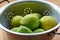 Lemon fresh. a colander filled with green lemons on a kitchen table.