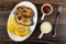 Lemon, fried steak from salmon in dish, sauce boats with ketchup and mayonnaise, fork on wooden table. Top view