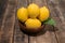 Lemon pile in bowl has leaves on wood background close up.