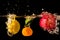 A lemon, tangerine and apple are splashing into water in black background