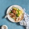 Lemon thyme baked chicken, potatoes and green peas on a white plate on a blue background.