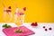 Lemonade with fresh raspberries in glasses with cocktail straws stands on a white table against the background of an orange wall.