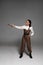 Length view of attractive steampunk woman standing with hand on hip and aiming with pistol on grey