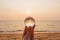 Lens ball in hand with reflection of sea and sunset on the beach