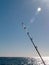 Lens flare across blue sky and fishing rod projecting over sea