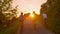 LENS FLARE: Unrecognizable cyclists pedal along the empty road at golden sunset.