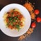 Lentil pasta with tomato sauce, parsley in a white plate on a dark table. Lentil beans on the side and cherry tomatoes