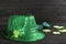 Leprechaun`s hat and decorative clover leaves on black wooden background. St. Patrick`s day celebration