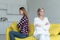 Lesbian females couple in casual clothes sitting back to back with crosed hands on yellow sofa after quarrel