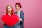Lesbians hold a red heart at the breast level on the left on a pink background